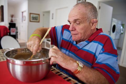 A man in a red and blue striped shirt mixing ingredients in a bowl with a wooden spoon.