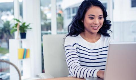 A woman with shoulder length hair smiling while sitting at a computer typing