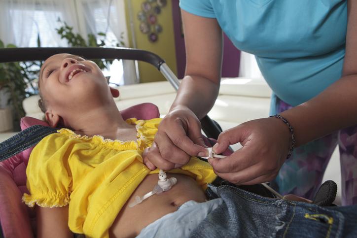 Support worker adjusting PEG feeding tube of a young girl